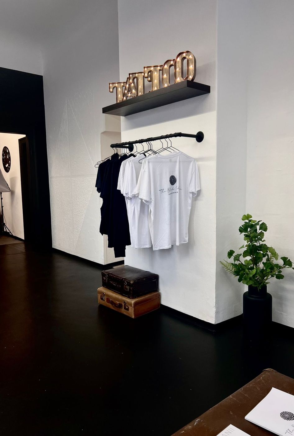 Leuchtschrift Tattoo über einer Kleiderstange mit Studio-Shirts